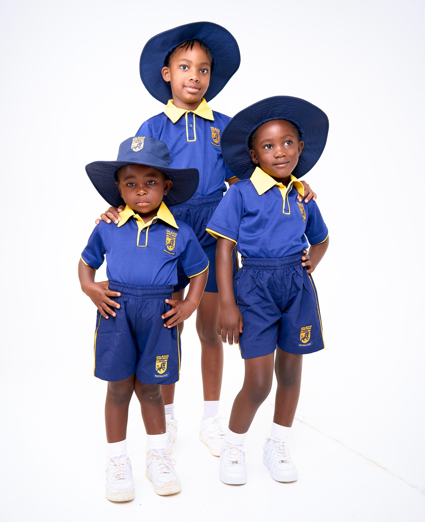 Three children in Gilead Advent School navy and gold summer uniforms with wide-brim sun hats, manufactured by NECST