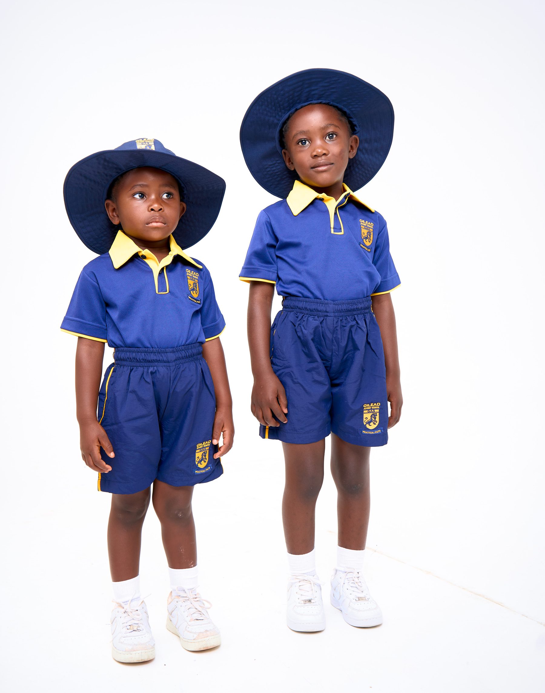 Two children wearing navy summer uniform shorts and polo shirts with sun hats