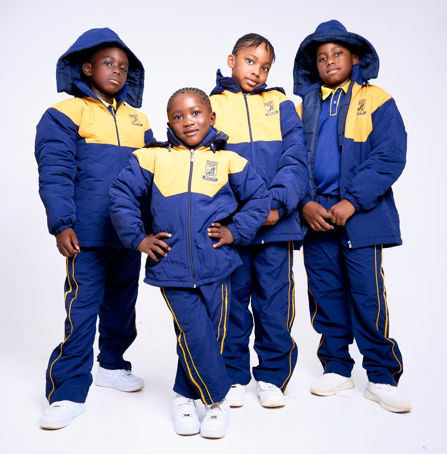 Four schoolchildren wearing navy and gold NECST winter tracksuits with hoods
